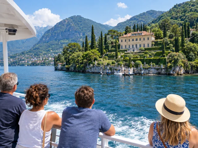 Passengers on a Lake Como ferry deck looking at a lakeside villa